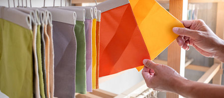 Stylist hand comparing fabric pieces from fabric swatch material. Upholstery sample collection hanging on showcase rack. Textile industry for home interior design and furniture finishing decorの写真素材