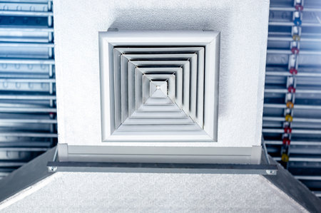 Air vent duct with metallic grill installed on the ceiling with electrical conduits wiring above. Ventilation system equipment for modern public buildingの写真素材