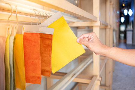 Stylist hand choosing yellow fabric piece from fabric swatch material. Upholstery sample collection hanging on showcase rack. Textile industry for home interior design and furniture finishing decorの写真素材