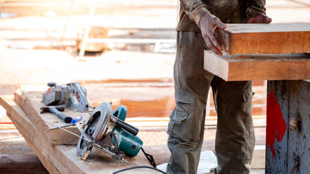 Male carpenter setting workbench preparing work tools for cutting and planing timber. Electric circular saw with planer and hammer on wooden plank at construction site. Lumber industry conceptの写真素材