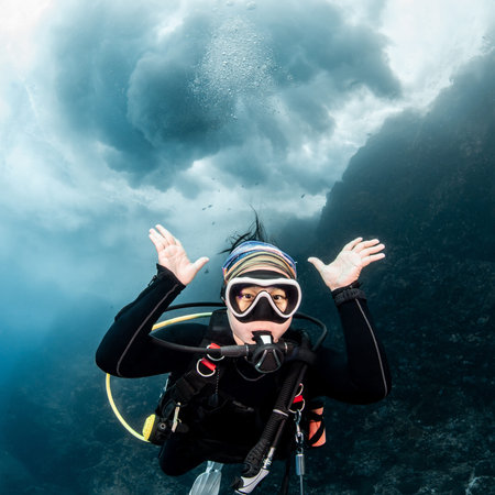 Asian female scuba diver looking at camera posing with the stunning wave breaking exploding above...
