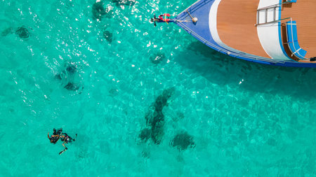 Aerial view of two scuba divers floating on the surface over turquoise crystal clear water near the boat at Koh Racha Island, A popular destination for summer activity in Phuket, Thailand.の写真素材
