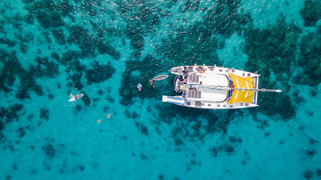 Aerial top view of sailing catamaran anchor over turquoise water with tourists swimming and paddle boarding at Racha Yai Island, A popular destination for summer vacation in Phuket, Thailand.の写真素材