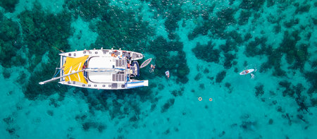 Aerial top view of sailing catamaran anchor over turquoise water with tourists swimming and paddle boarding at Racha Yai Island, A popular destination for summer vacation in Phuket, Thailand.の写真素材