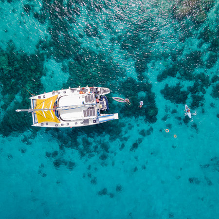 Aerial top view of sailing catamaran anchor over turquoise water with tourists swimming and paddle boarding at Racha Yai Island, A popular destination for summer vacation in Phuket, Thailand.の写真素材