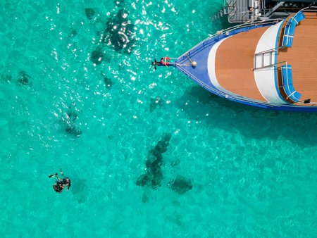 Aerial view of two scuba divers floating on the surface over turquoise crystal clear water near the boat at Koh Racha Island, A popular destination for summer activity in Phuket, Thailand.の写真素材