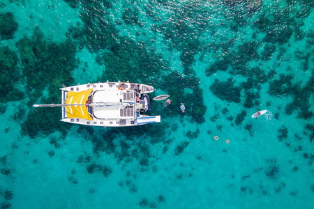 Aerial top view of sailing catamaran anchor over turquoise water with tourists swimming and paddle boarding at Racha Yai Island, A popular destination for summer vacation in Phuket, Thailand.の写真素材