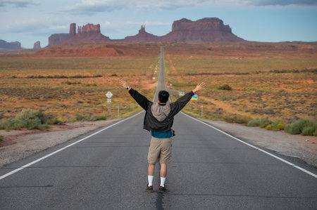 Rear view of Asian man tourist standing on highway US route 163 looking at the long road view leading to Monument Valley on the Arizona-Utah border, United States. America road trip travelの写真素材