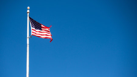 Flag of United States (USA) or American flag waving in breeze against the blue sky symbolizing US memorial day or 4th of July Independence dayの写真素材