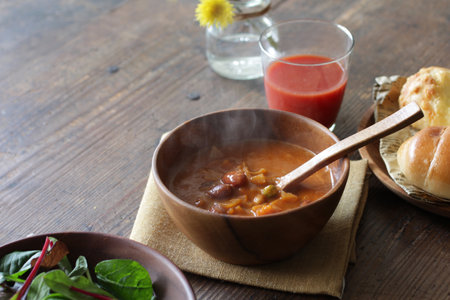 Bowl of vegetable soup with bread and tomato juice on wooden tableの写真素材