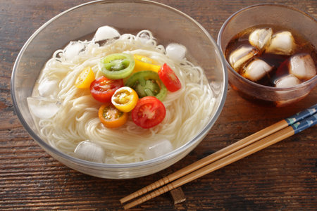 Somen noodles in a glass transparent bowl with cherry tomatoes on a wooden grain boardの写真素材