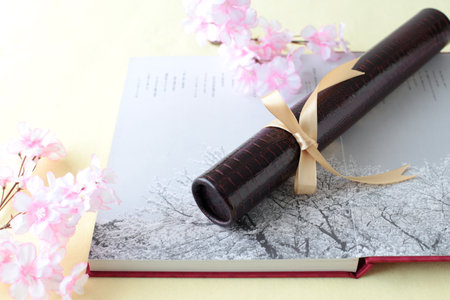 Graduation certificate, graduation album and cherry blossom petalsの写真素材