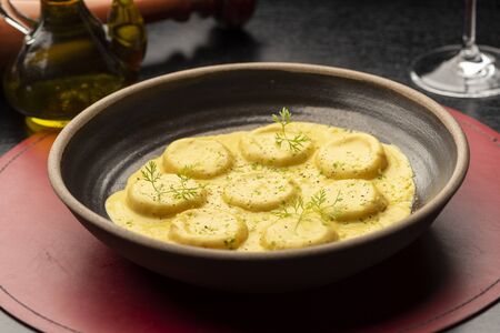 Ravioli pasta egg yolk raviolo stuffed with sauce gravy on leather mat wooden table olive oil bottleの写真素材