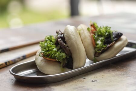 two asian bao stuffed with lettuce vegetables and pork belly on a wooden table and chopsticksの写真素材