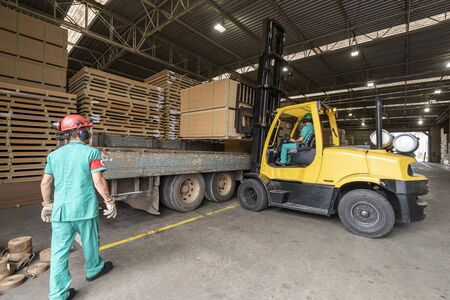 wood pallet forklift driving at a factory floor inside a shed loading a truckの写真素材