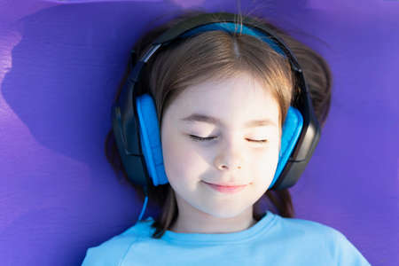 Little girl closed her eyes listening to music with headphones lying on a purple rugの写真素材