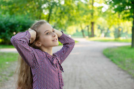 A posing girl 11 years old on a road in a park. Against a background of trees and grass. Front viewの写真素材