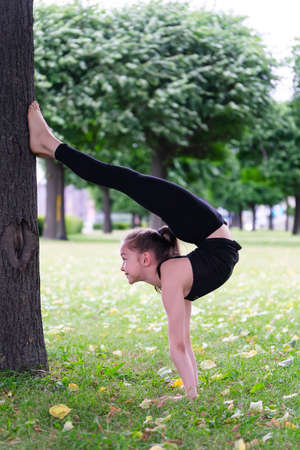 Girl gymnast performs her exercises in the park on the grass by a tree. Series of photosの写真素材