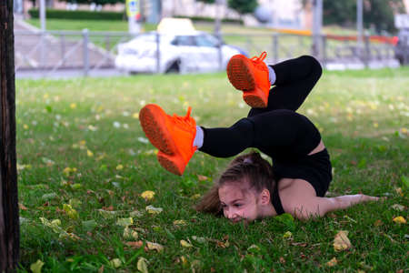 A girl of school age doing gymnastics in a park on the grass. Series of photosの写真素材
