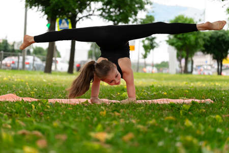 A girl of school age doing gymnastics in a park on the grass. Series of photosの写真素材