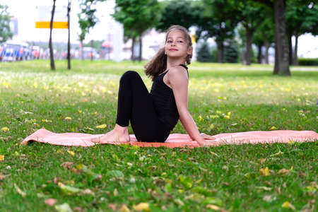 Gymnast schoolgirl warming up in a grass park before performing complex exercises. Series of photosの写真素材