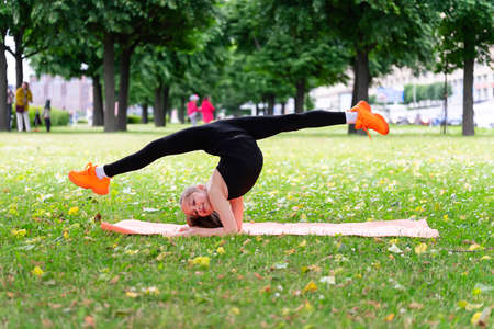 A girl of school age doing gymnastics in a park on the grass. Series of photosの写真素材