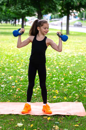 A schoolgirl takes care of blue chicken dumbbells in a park on the grass. Series of photosの写真素材