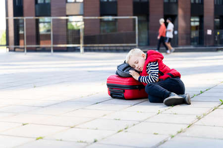 Tired little boy traveler on the background of modern buildings lies on a suitcase. Front viewの写真素材
