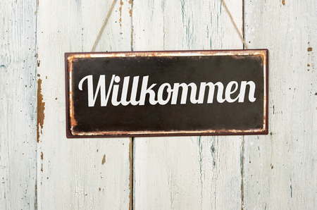 Old metal sign in front of a white wooden wall - German word for Welcome- Willkommenの写真素材