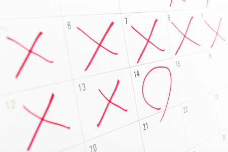 close up of a white calendar page with some of the days crossed off with a red Xの写真素材