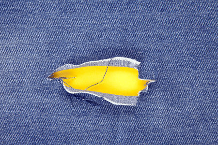 Hole in denim jeans with yellow background