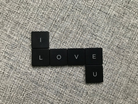 Word I Love U text on black square tiles on grey fabric background, Love concept