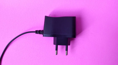 Black power plug on a pink background. Close-up photo.