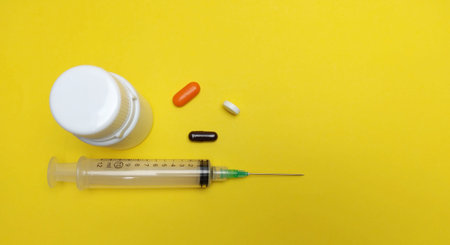 Syringe and pills on yellow background. Copy space for text.