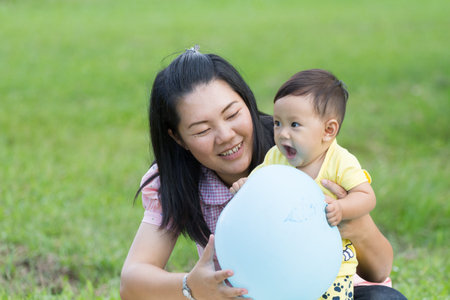 mother happy  to hold son for play blue balloon in park