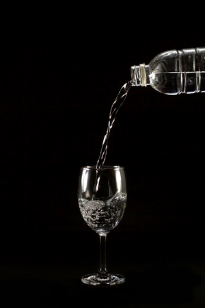 drop drink water from plastic bottle into glass on black blackgroundの写真素材