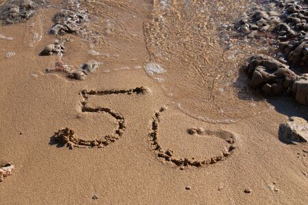 5G written on the sandy beach with sea wavesの写真素材