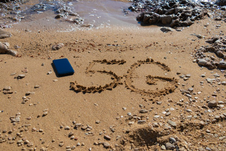 5G written on the sandy beach with sea waves and cellphoneの写真素材