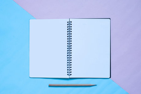 Top view of notebook and pencil on blue and pinl pastel color bakcground