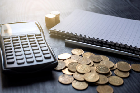 Close up gold coins, calculator, pen, notebook on black table. Business, finance, marketing,...