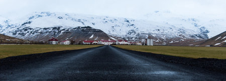 Empty road leading to small town with snowy mountains in background, Iceland Winter time