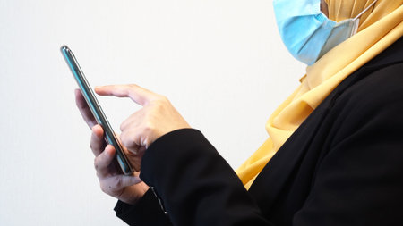 A hijab women wearing a mask and holding a smartphone. Suitable for back to work in new norm concept