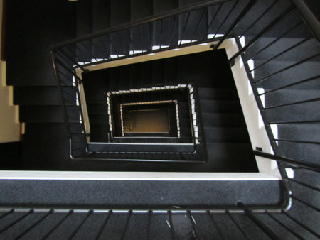 Hypnotic square spiral staircase creating infinite depth perspective. Dark industrial design with...