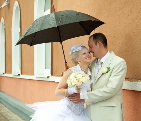 Happy bride and groom embracing under an umbrellaの写真素材