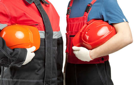 Two builders or industrial workers in uniform holding hardhats isolated on whiteの写真素材
