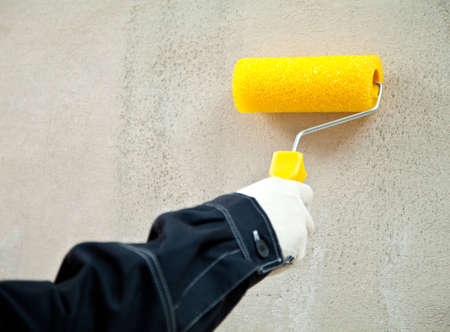 Working with paint roller; closeup of hand holding paint roller against the wallの写真素材