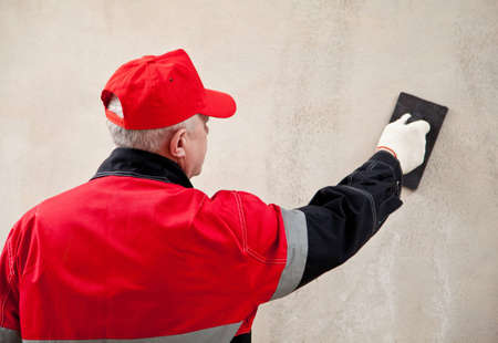 Back view of a plasterer in uniform working with float against the wallの写真素材