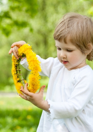 Adorable little girl holding yellow chaplet made of dandelionsの写真素材
