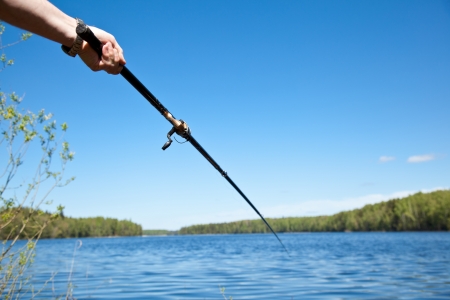 Hand holding fishing rod over the waterの写真素材