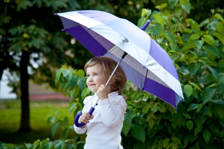 Cute little girl with umbrella in a summer parkの写真素材